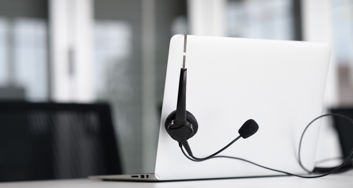 White laptop with a black call center headset hanging from its back on an office desk