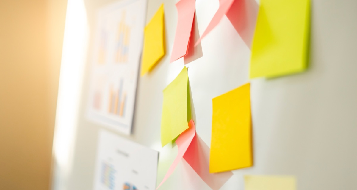 Yellow, pink and green sticky notes stuck to a whiteboard beside printed charts in a sunlit office