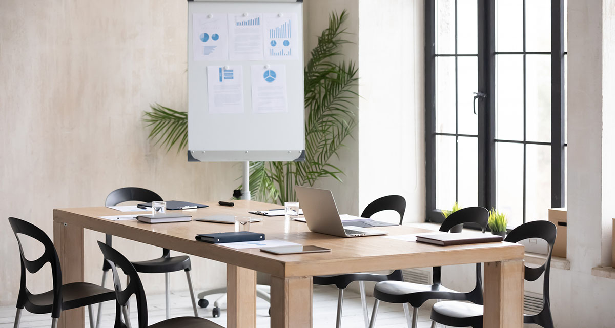 Empty conference room with a wooden table set with laptops, notebooks and water glasses in front of a flip chart pinned with printed charts